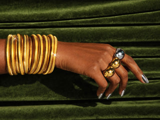 Elorae hand model wearing gold Metropolis Coil Bangles and Metropolis silver and gold Halo rings on a green velvet background.