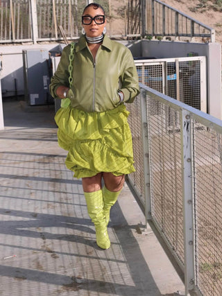 Tati Baker wearing Elorae's silver Metropolis Torque choker set, matching silver Coil Bangles, and silver Loop Earrings with a green jacket, skirt and matching boots.