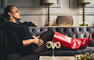 Tati Baker sitting in Elorae's gold and silver jewelry on grey couch in luxury interior.