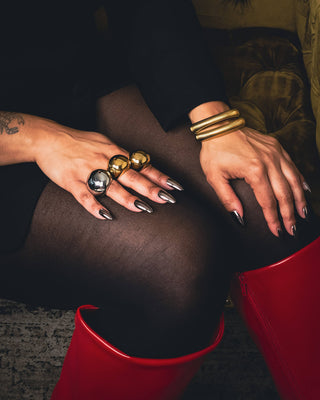 Close up of Tati Baker posing in black outfit wearing Elorae gold and silver Halo Rings and gold Metropolis Coil Bangles.